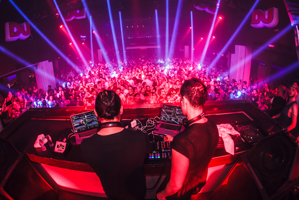 DJs playing to a packed club under red and blue lights
